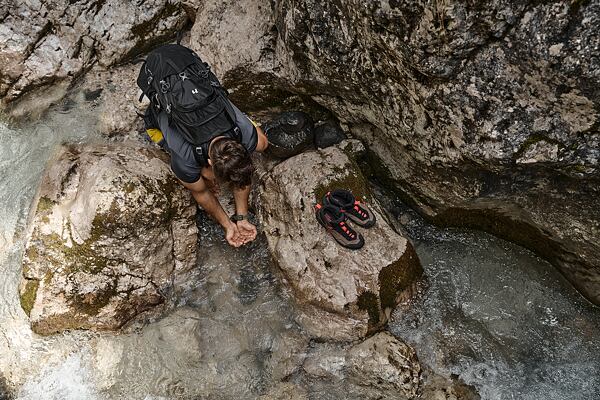 Muž na treku si nabírá vodu z potoku