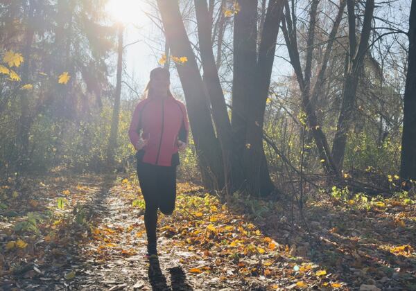 Žena v červené podzimní bundě běží lesní cestou
