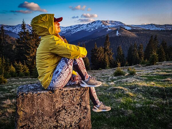 Žena ve žluté podzimní bundě sedí na kameni