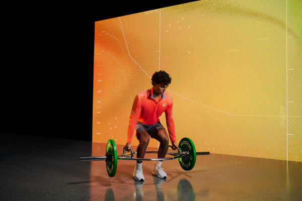 Muž v oranžové sportovní mikině Under Armour zvedá činku